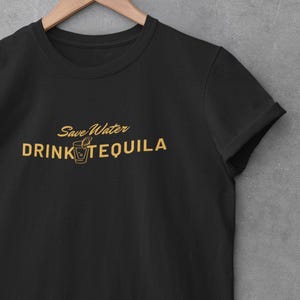 May include: Black t-shirt with a gold graphic that says "Save Water Drink Tequila" with a small image of a shot glass with a lime wedge.