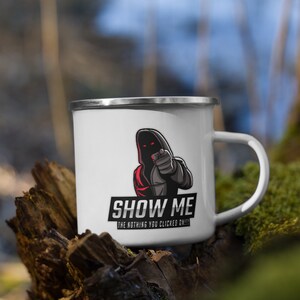 Pode incluir: Caneca de esmalte branco com uma ilustração em preto e vermelho de uma figura encapuzada apontando o dedo para o espectador. O texto "SHOW ME THE NOTHING YOU CLICKED ON!!!" está impresso abaixo da ilustração.