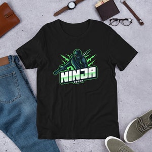 Könnte beinhalten: Schwarzes T-Shirt mit einem Ninja-Motiv und dem Text "NINJA CODER" in Weiß und Grün. Der Ninja ist schwarz und hält ein Schwert, vor einem grünen Blitz-Design. Das T-Shirt besteht aus einem weichen Material.