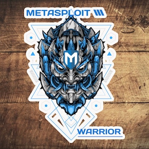 Op de afbeelding: Een gestileerde blauwe en grijze illustratie van een krijgersgezicht met een geometrisch patroon erachter. Het krijgersgezicht heeft een grote, scherpe neus en een wijd open mond. De tekst "METASPLOIT" staat boven het krijgersgezicht, en de tekst "WARRIOR" staat onder het krijgersgezicht.