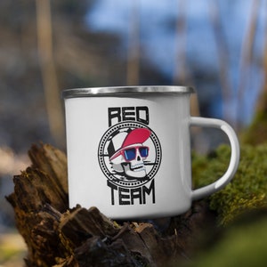 Op de afbeelding: Witte emaille campingmok met een zwart-witte schedelgrafiek die een rode baseballpet en een zonnebril draagt. De tekst "RED TEAM" is onder de schedel gedrukt.
