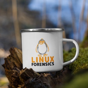 Może przedstawiać: Biały kubek emaliowany ze srebrną obwódką i uchwytem. Kubek przedstawia pomarańczowo-czarną ilustrację pingwina oraz napisy "LINUX FORENSICS" w kolorze pomarańczowym i czarnym. Kubek stoi na kawałku drewna.