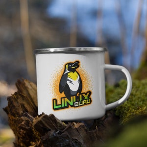 Peut inclure: Mug en émail blanc avec un bord et une anse argentés. Le mug présente un graphisme de pingouin avec des accents jaunes et noirs, sur fond orange. Le texte "LINUX GURU" est en dessous.