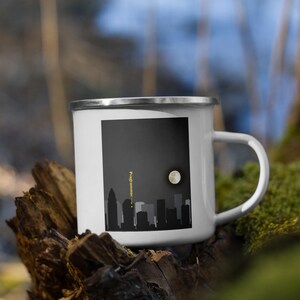 May include: White enamel mug with a black and white cityscape silhouette and a full moon. The text "Programm" is written vertically on the side of the mug.