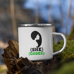 Könnte beinhalten: Weiße Email Tasse mit einer schwarzen Silhouette eines Frauenkopfes und dem Text "{SHE} [CODES];" in Grün.