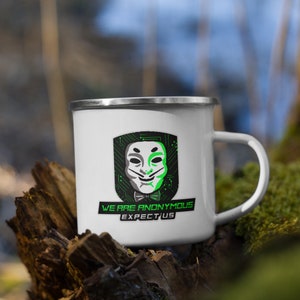 Könnte beinhalten: Weiße Emailtasse mit einer schwarzen und grünen Grafik der Anonymous-Maske und dem Text "We Are Anonymous Expect Us".
