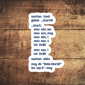 Puede incluir: Un primer plano de una superficie de madera con una pegatina blanca que contiene código de ensamblaje. El código incluye el texto "Hello World!" y las instrucciones "mov edx, len", "mov ecx, msg", "mov ebx, 1", "mov eax, 4", "int 0x80", "mov eax, 1", "int 0x80", "section.data", "msg db "Hello World!"