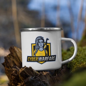 Könnte beinhalten: Weiße Emailtasse mit einem gelben und blauen Logo, das eine Frau mit einem Gewehr zeigt. Das Logo lautet "Cyber Warfare".