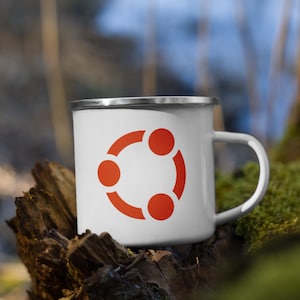 Puede incluir: Taza de esmalte blanco con un logotipo de círculo rojo que presenta tres círculos conectados. La taza está sentada sobre un trozo de madera desgastada.