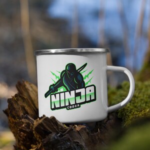 May include: White enamel mug with a green and black ninja logo. The logo says "Ninja Coder".