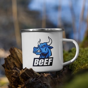 Puede incluir: Taza de camping de esmalte blanco con una ilustración de un toro azul y la palabra "BEEF" impresa en negro.