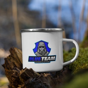 Könnte beinhalten: Weiße Emaille-Campingtasse mit einem blau-weißen Logo, auf dem "Blue Team Defense by Offense" steht. Das Logo zeigt eine Person mit Kapuze, die ein blaues Bandana und eine Sonnenbrille trägt.