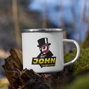 May include: White enamel mug with a black and red illustration of a man in a top hat and monocle. The text "JOHN THE RIPPER" is printed in yellow below the illustration.