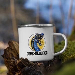 May include: White enamel camping mug with a blue and yellow snake graphic and the text "CODE-BLOODED".