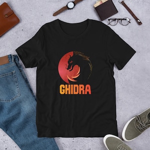 Könnte beinhalten: Schwarzes T-Shirt mit einem roten, orangefarbenen und gelben Grafik eines Drachen mit dem Text "GHIDRA" darunter.