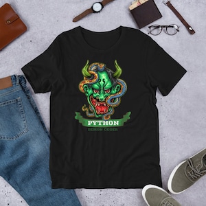 Peut inclure: T-shirt noir avec un visage de démon vert entouré d'un serpent. Le texte "PYTHON DEMON CODER" est situé sous l'image.