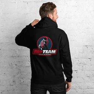 Peut inclure: Sweat-shirt à capuche noir avec un motif rouge et bleu d'une figure masquée avec le texte "RED TEAM DEFENSE BY OFFENSE"