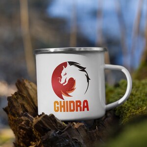 Könnte beinhalten: Weiße Emaille-Tasse mit einem roten, orangefarbenen und gelben Drachenlogo und dem Text "GHIDRA" in Orange.