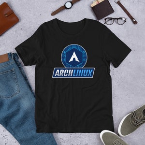 Könnte beinhalten: Schwarzes T-Shirt mit einem blau-weißen Arch Linux Logo. Das Logo zeigt ein stilisiertes A in einem Hexagon mit einem Schaltkreisdesign. Der Text "Arch Linux" befindet sich unter dem Logo in einem weißen Rechteck mit blauem Rahmen.