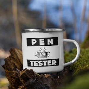 Könnte beinhalten: Eine weiße Emailletasse mit einem schwarz-weißen Design. Die Tasse trägt den Text "PEN TESTER" und eine Grafik eines Computers mit einem Schädel darin. Die Tasse steht auf einem Stück Holz.