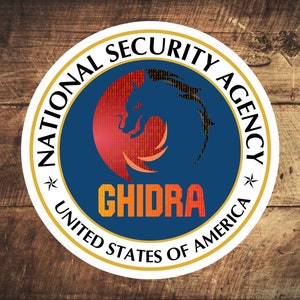 Op de afbeelding: Een blauwe en witte ronde zegel met een gouden rand. De zegel heeft een rode en oranje draak erin met de tekst "NATIONAL SECURITY AGENCY" en "GHIDRA" in het midden. De tekst "UNITED STATES OF AMERICA" staat onderaan de zegel.