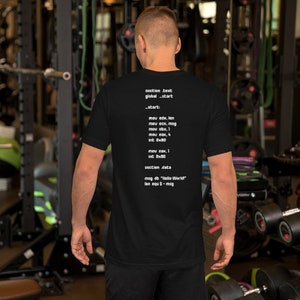 May include: A black t-shirt with white text on the back. The text is assembly code, which is a low-level programming language. The code includes the following lines: section .text, global start, _start: mov edx, len, mov ecx, mag, mov ebx, 1, mov eax, 4, int 0x80, mov eax, 1, int 0x80, section data, mag db "Hello World!", len equ $-mag