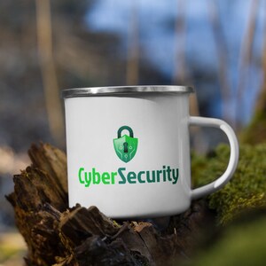 Könnte beinhalten: Eine weiße Emailletasse mit einem grün-blauen Logo eines Vorhängeschlosses mit Platinen-Design und dem Text "CyberSecurity".