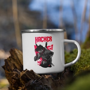 Könnte beinhalten: Weiße Emailtasse mit einer roten und schwarzen Illustration einer maskierten Figur, die ein Schwert hält. Der Text "HACKER" ist in roten Buchstaben über der Illustration gedruckt.