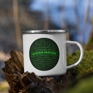 Könnte beinhalten: Weiße Emailtasse mit einem schwarzen Kreis, der grünen Binärcode und den Text "SYSTEM FAILURE" enthält.