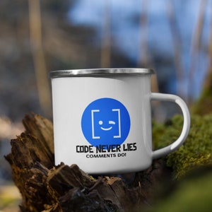 May include: White enamel mug with a blue square and a winking face. The text "CODE NEVER LIES COMMENTS DO!" is printed below the square.