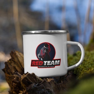 Könnte beinhalten: Weiße Emaille-Campingtasse mit einem rot-weiß-schwarzen Logo, auf dem "Red Team" und "Defense by Offense" steht. Das Logo zeigt eine maskierte Figur mit einer roten Hand vor dem Gesicht.