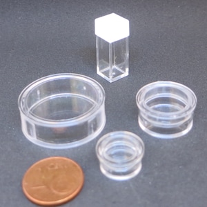 以下が含まれることがあります： 小さな透明なプラスチック容器と1セント硬貨のコレクション。容器はサイズと形状が異なり、白い蓋が付いた背の高い長方形の容器と、いくつかの丸いオープン容器が含まれます。硬貨は銅色です。