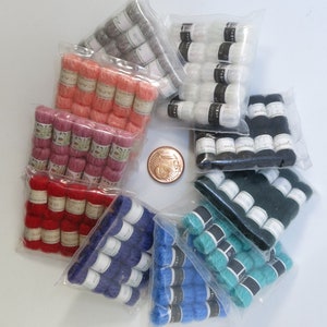 May include: Assortment of colourful yarn in individual plastic bags. The yarn is in shades of red, pink, blue, green, black, and white. Each bag contains multiple spools of yarn.