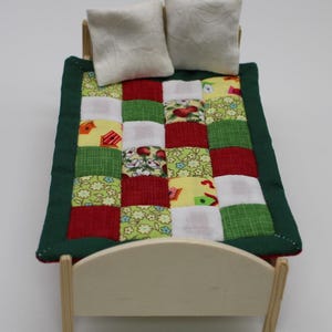 Op de afbeelding: Een miniatuur houten bed met een groen en rood patchwork dekbed en twee witte kussens.