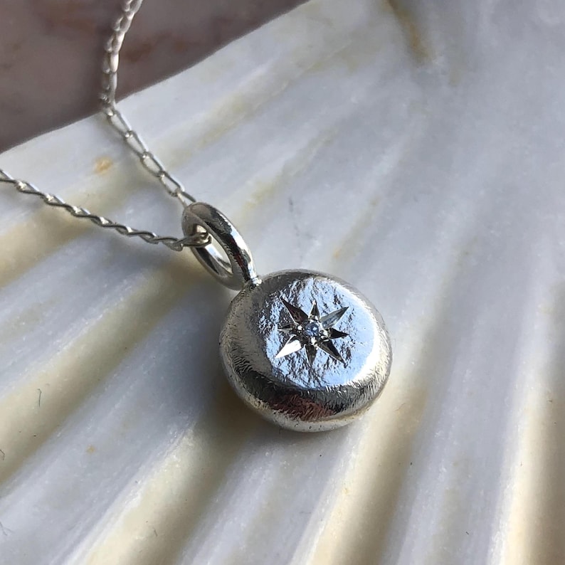 May include: A silver necklace with a round pendant featuring a five-pointed star with a small diamond in the centre.