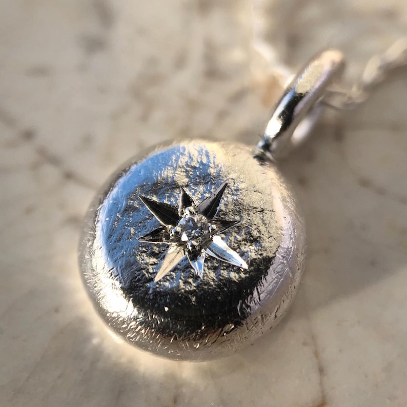 May include: A silver pendant necklace with a round, textured charm featuring a small diamond set in a star shape.
