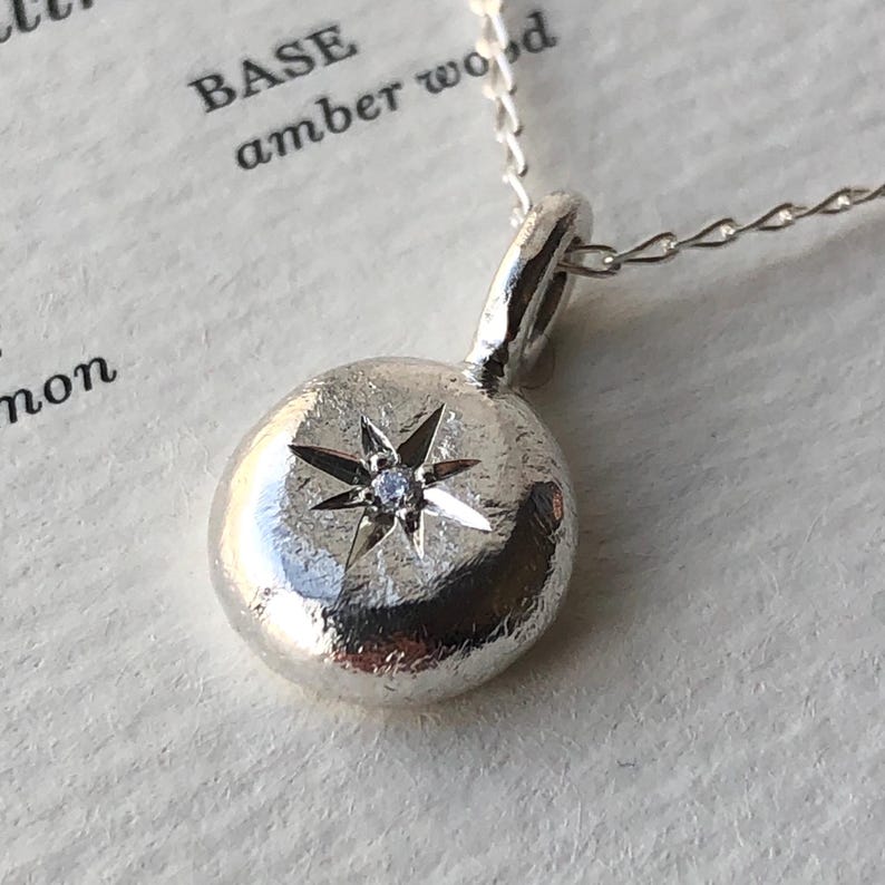 May include: A silver necklace with a round pendant featuring a five-pointed star with a small diamond in the centre.