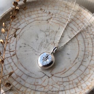 May include: A silver necklace with a round pendant featuring a small diamond set in a star shape.