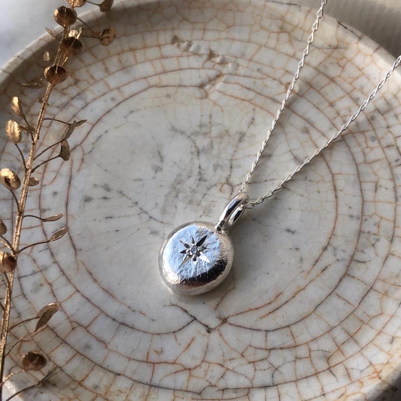 May include: A silver necklace with a round pendant featuring a small diamond set in a star shape.