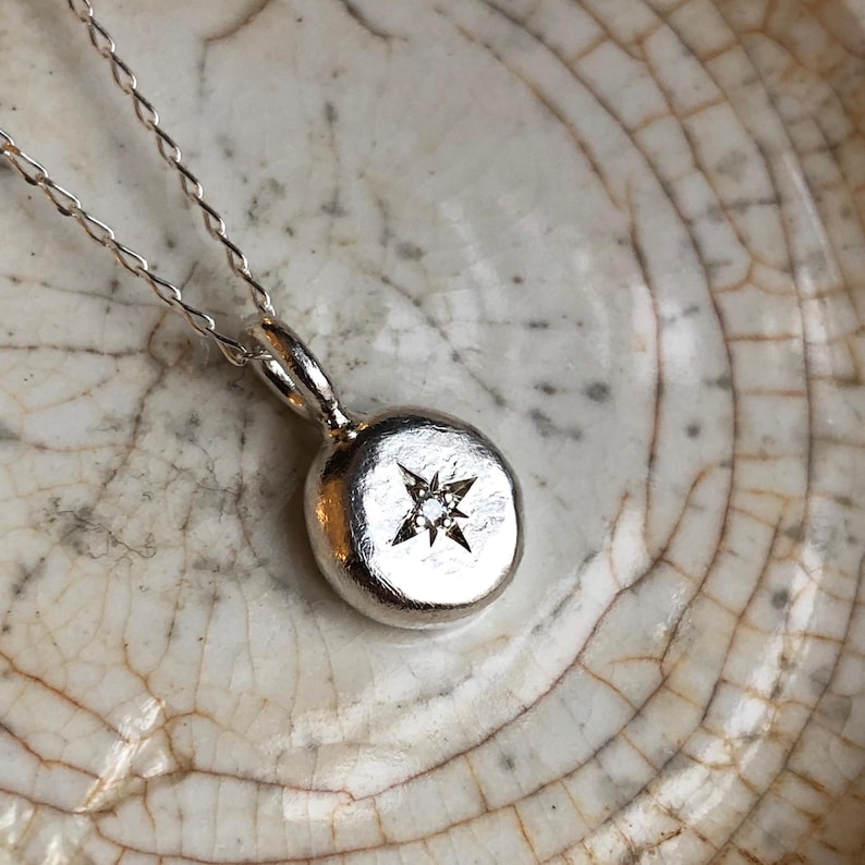 A recycled silver hand forged round pendant featuring a hand engraved star with 1.5mm lab grown diamond set in the centre. An ideal gift for the North Star in your life.