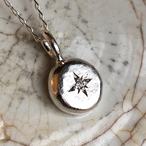 May include: A silver necklace with a round pendant featuring a small diamond set in a star shape.