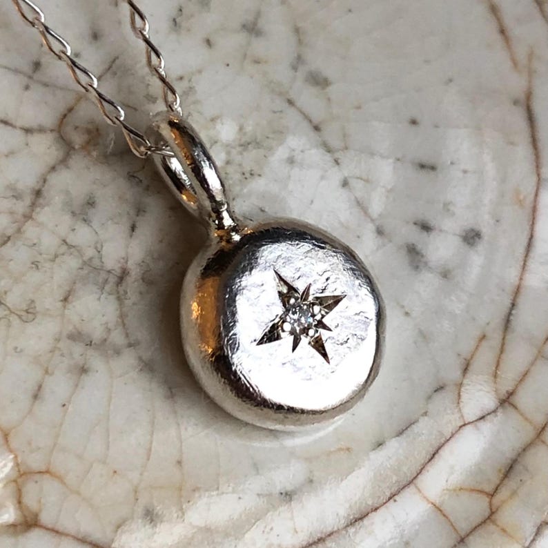 May include: A silver necklace with a round pendant featuring a small diamond set in a star shape.
