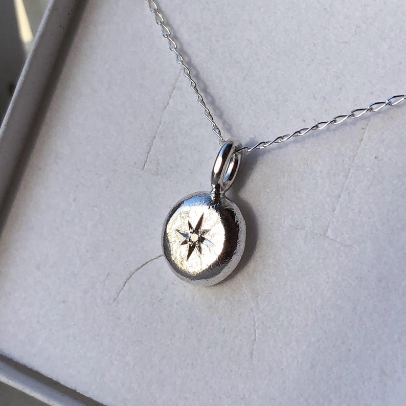 May include: A silver necklace with a round pendant featuring a small diamond in the centre, forming a star shape.