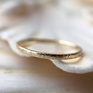 May include: A thin gold band ring with a textured surface.