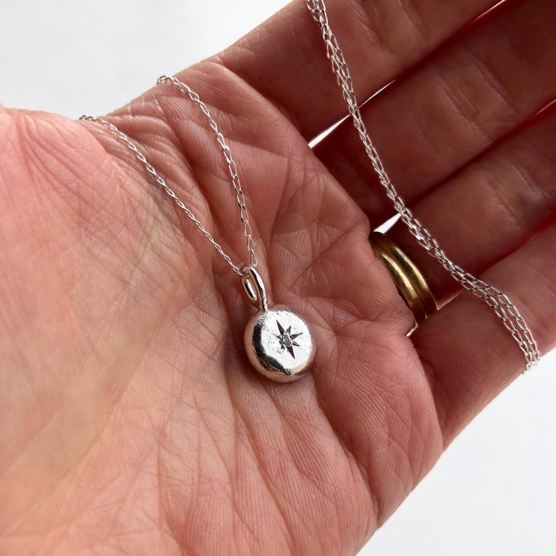 May include: A silver necklace with a round pendant featuring a small diamond in the shape of a star.