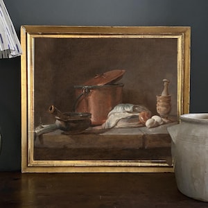May include: A framed still life painting featuring a copper pot with a lid, a mortar and pestle, and several eggs. The painting has a warm color palette with a gold frame. The painting is displayed on a wooden surface.