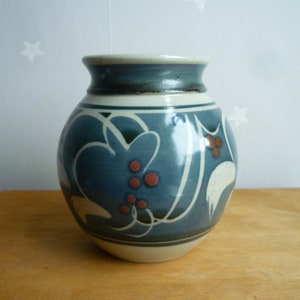 May include: A blue and white ceramic vase with a floral design. The vase has a round body and a narrow neck. The floral design features white leaves and red berries.