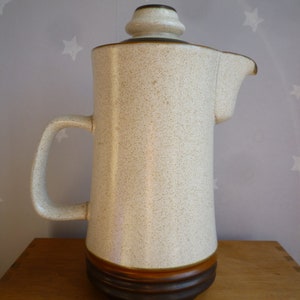 May include: A white ceramic jug with a brown rim and base. The jug has a speckled texture and a handle.