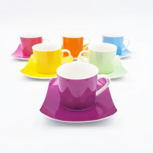 Può includere: Un set di sei tazzine da espresso in ceramica con piattini quadrati abbinati in colori vivaci tra cui viola, giallo, arancione, rosa, azzurro e verde chiaro. Ogni tazzina presenta un interno e un manico bianchi, disposte in modo sfalsato.
