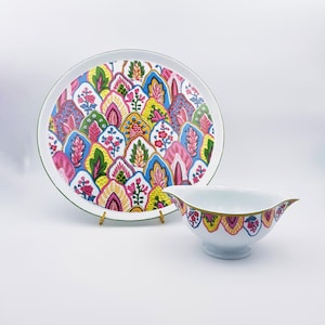 Peut inclure: Un ensemble décoratif comprenant un plat de service et un saucier. Le plat présente un fond blanc orné d'un motif floral coloré rose, bleu, jaune et vert. Le saucier présente un motif assorti et une bordure dorée.